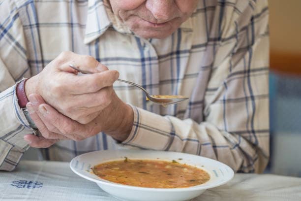 hombre mayor con Parkinson comiendo sopa